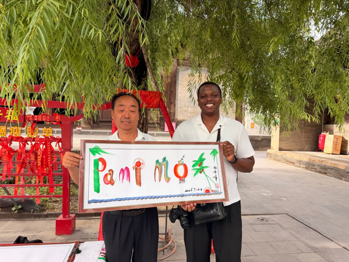 Pamimo and a street artist holding a painting of the name Pamimo, with letters made from bamboo, lanterns and palm leaves