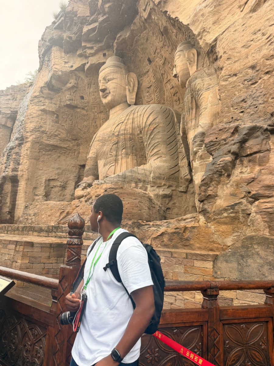 Pamimo looking up at a giant Buddha carved into a sandstone cliff at the Yungang Grottoes